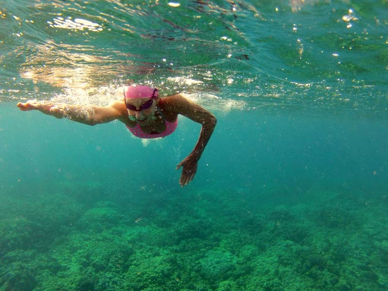 Open water swimmer photographed from below in clear green water